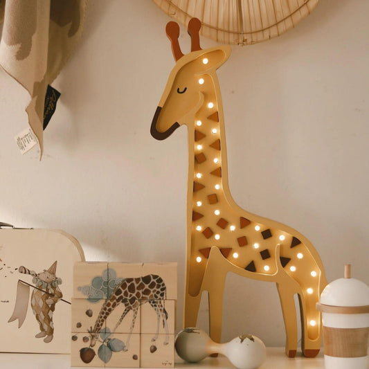 Decorative giraffe lamp with lights on a shelf with books and toys.
