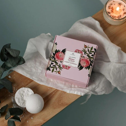 Bath bomb and decorative box with floral design on a wooden surface with a candle in the background.