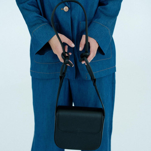 Person holding a black handbag against a light blue background