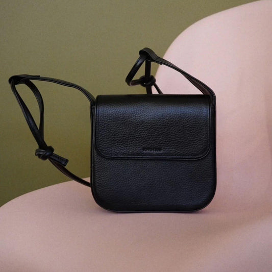 Black leather crossbody bag on a person's shoulder against a green background