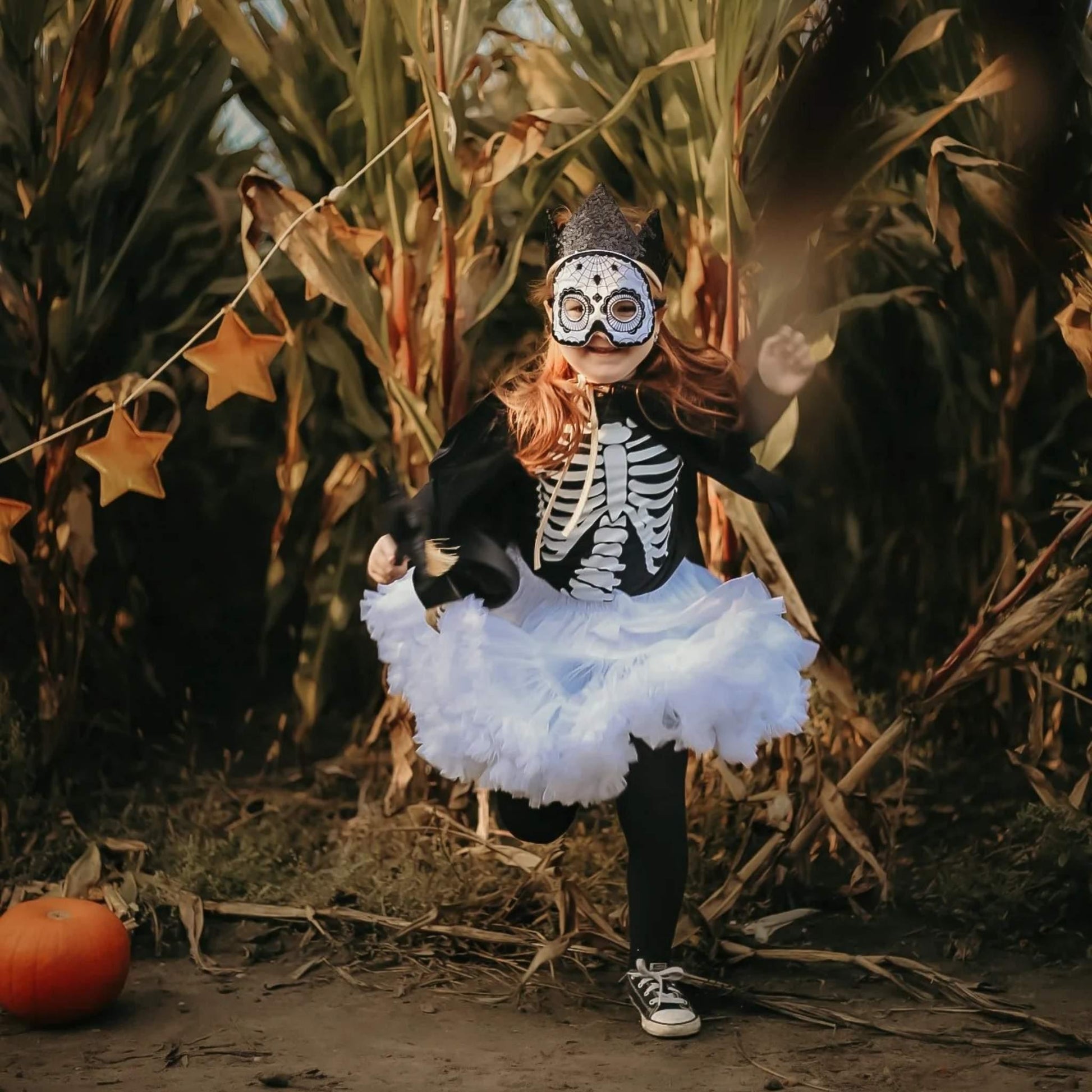 Child in a Halloween costume with a skeleton outfit and white tutu standing in a cornfield.