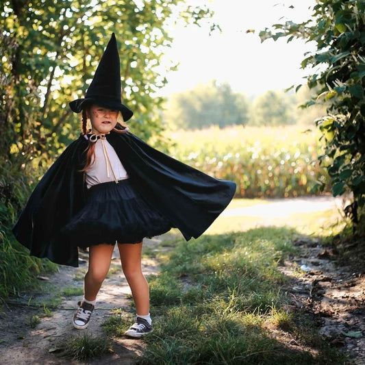 Child in a witch costume standing outdoors on a sunny day