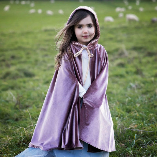 Young girl in a purple hooded cloak standing in a grassy field with sheep in the background