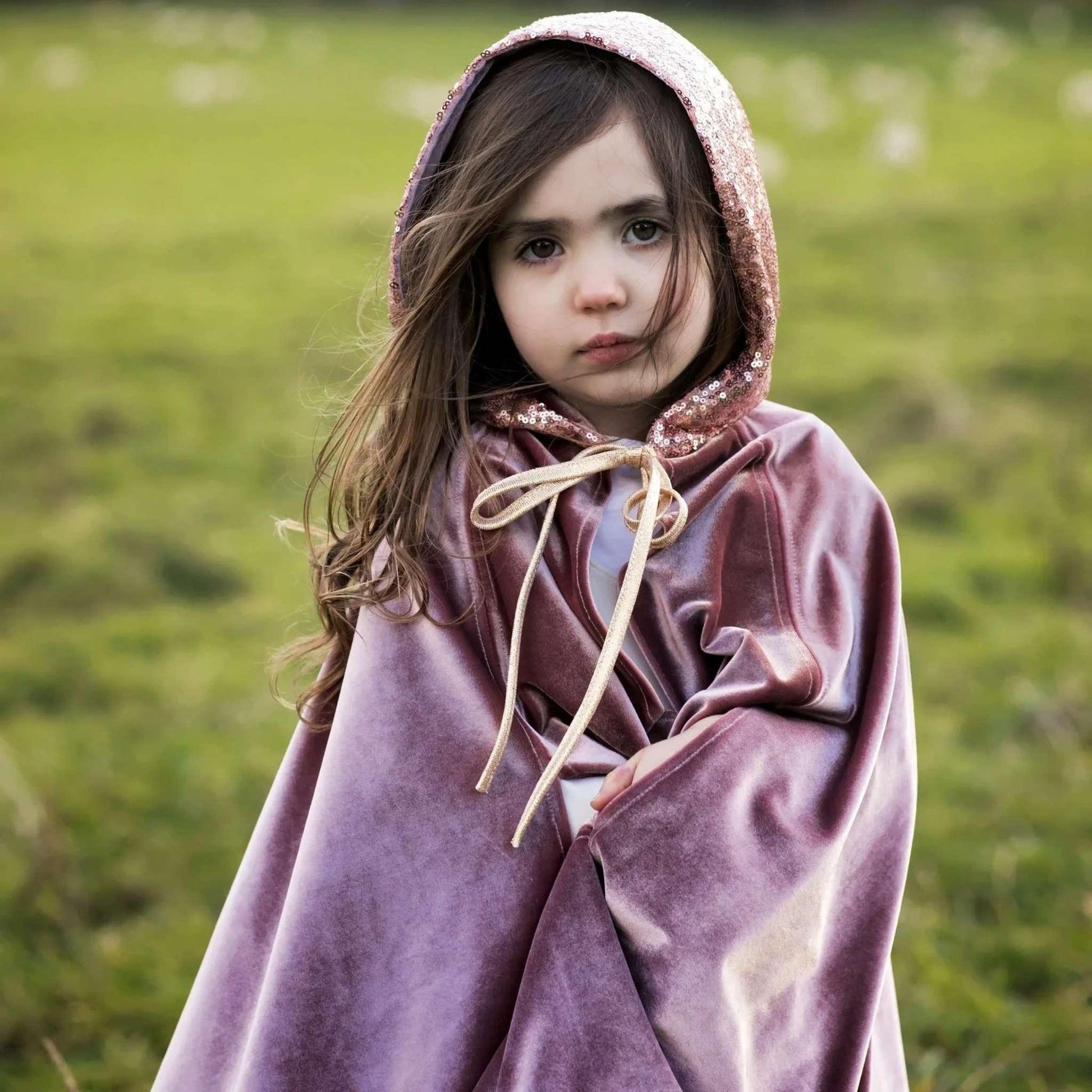 Child wearing a hooded cloak in a grassy field