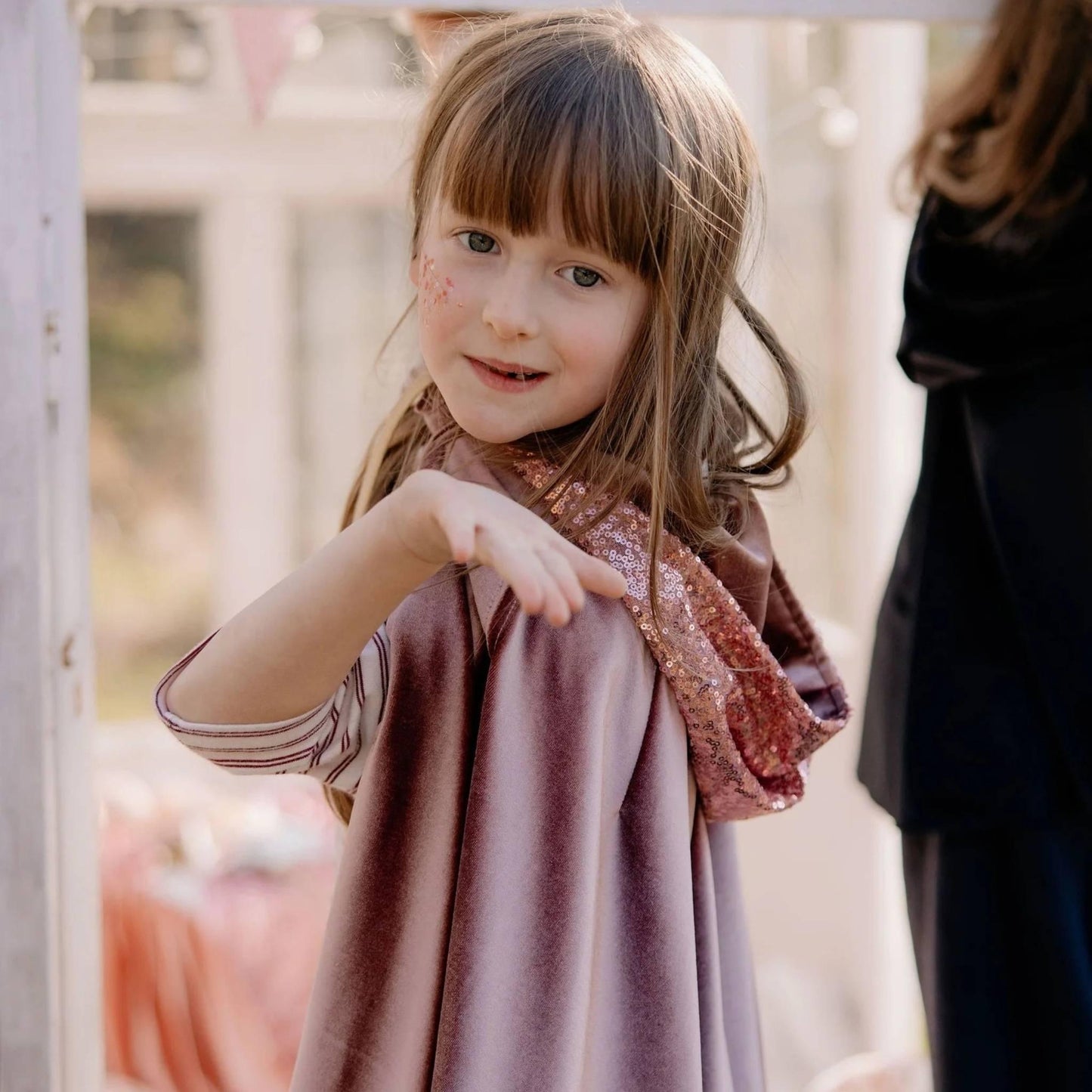 Young girl in a pink dress standing outdoors with a blurred background