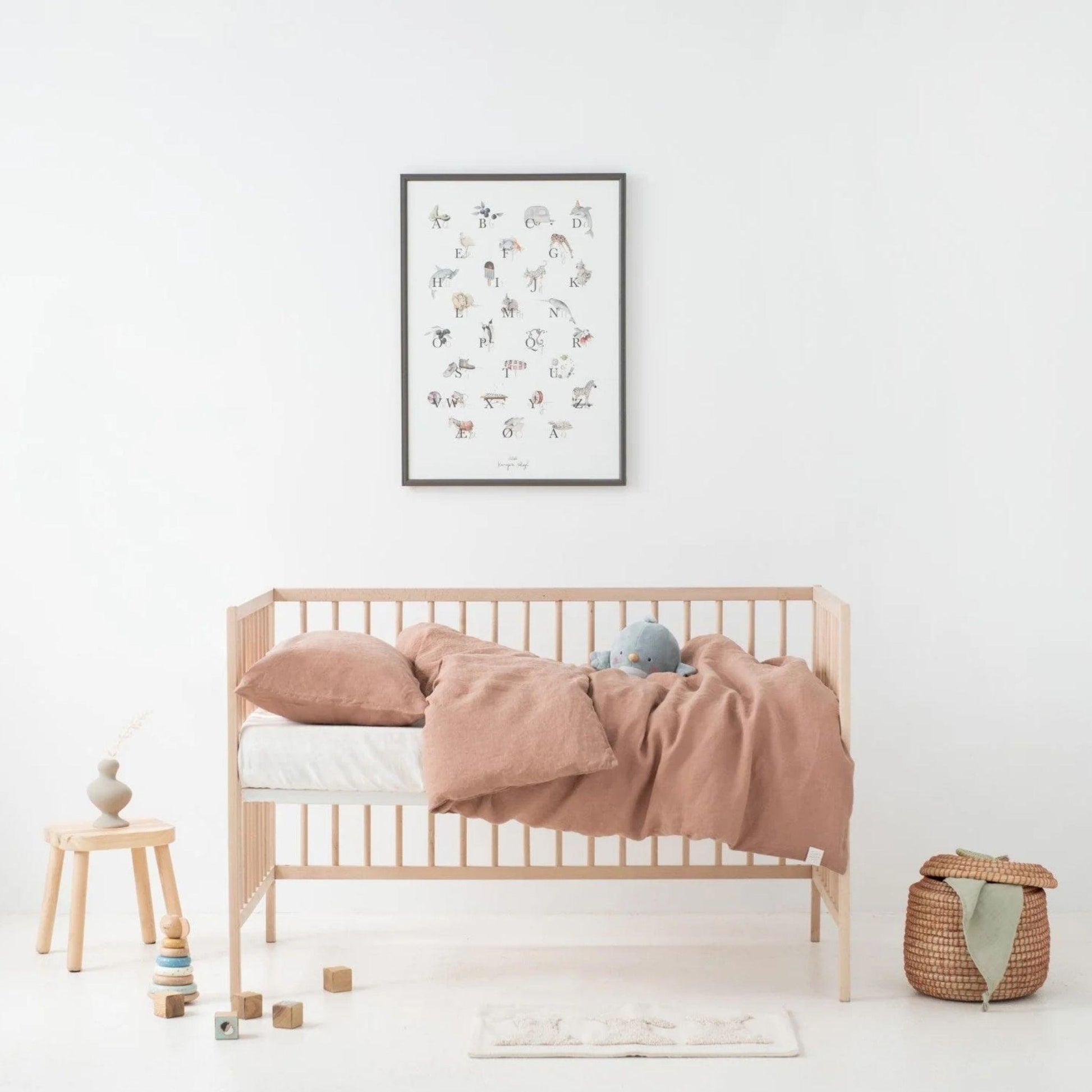 Nursery room with wooden crib, pink blanket, and framed artwork on a white wall.