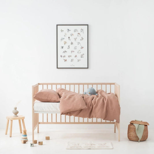 Nursery room with wooden crib, pink blanket, and framed artwork on a white wall.