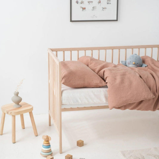 Nursery room with a wooden crib, pink bedding, and toys on a white floor.