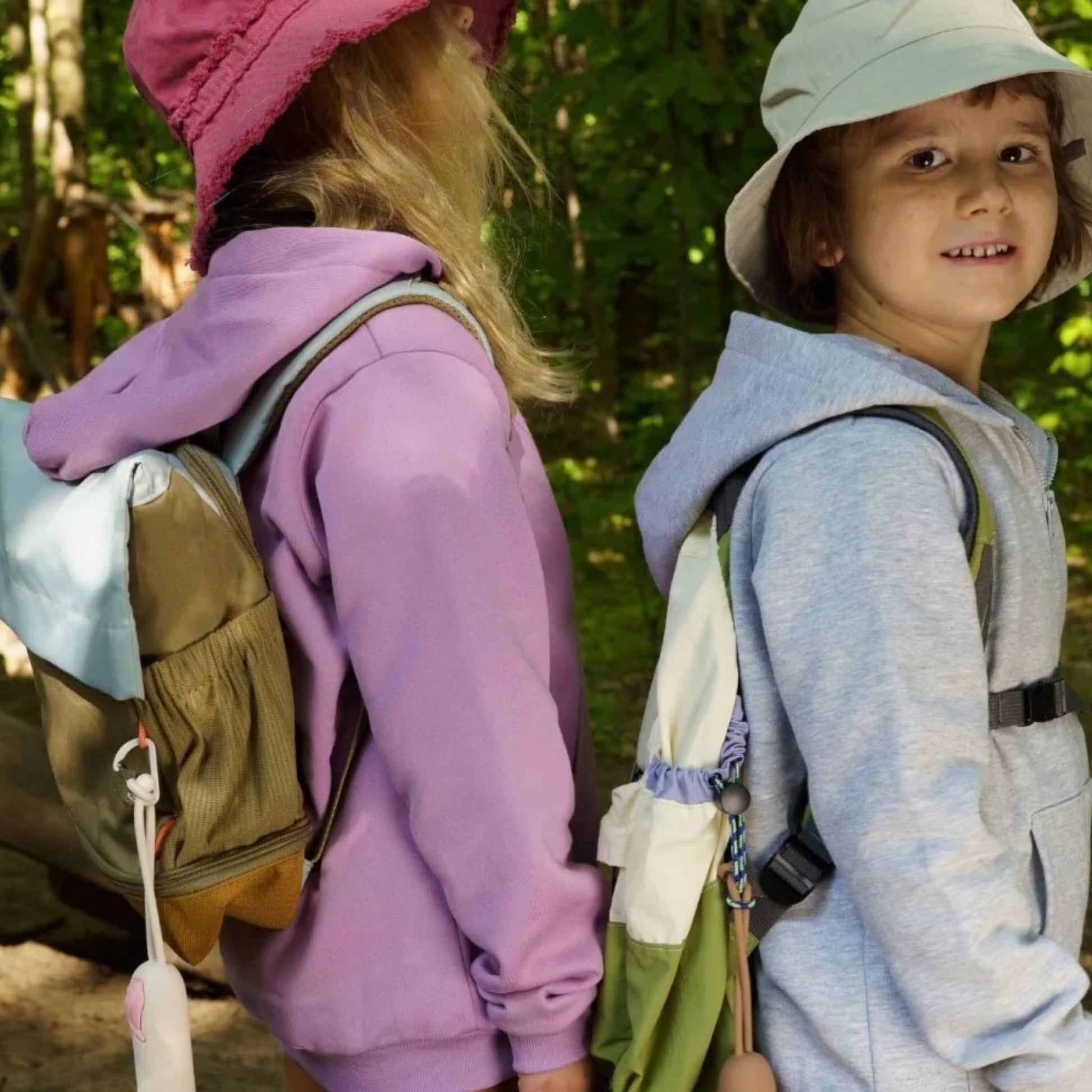 Two children in outdoor clothing with backpacks in a forest setting