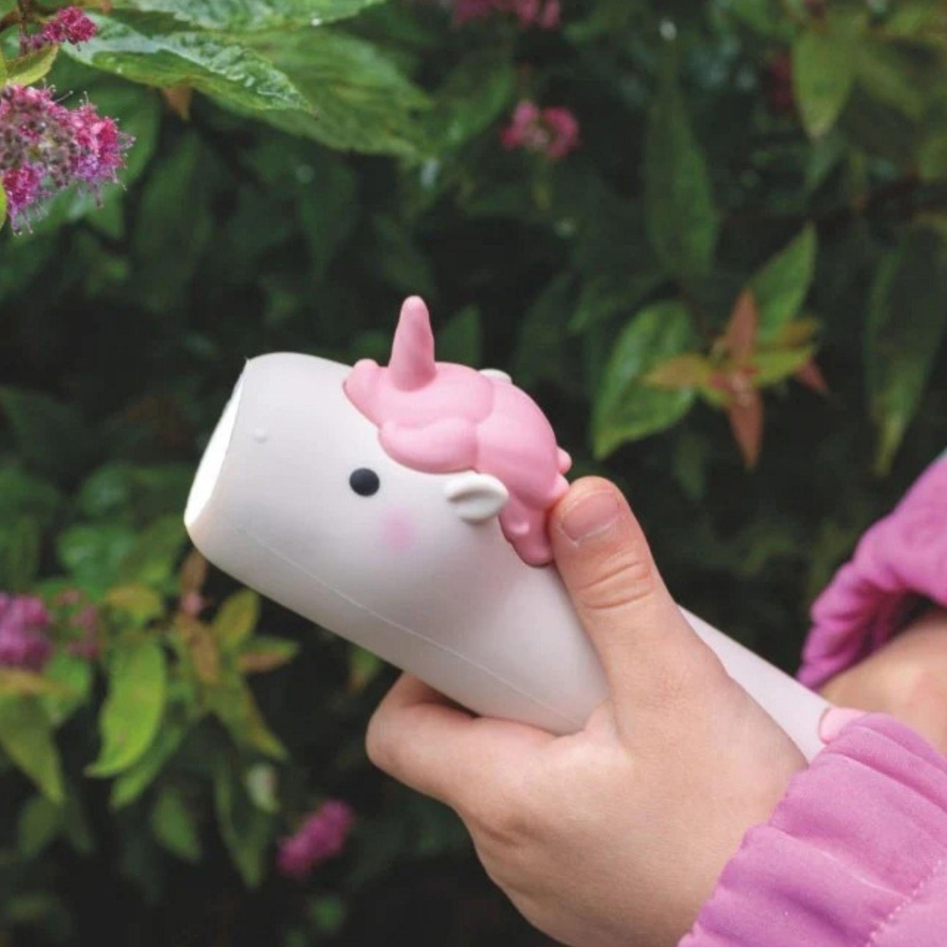 Hand holding a unicorn-shaped device with a blurred green and pink background