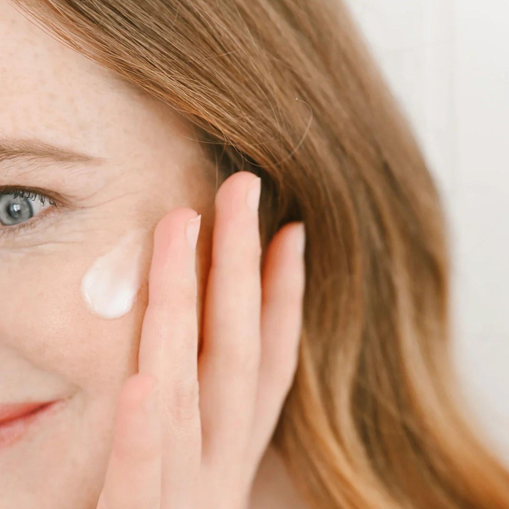 Woman applying cream to her face with a neutral background
