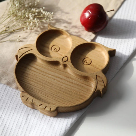 Wooden owl-shaped plate on a light surface with a cherry and flowers in the background